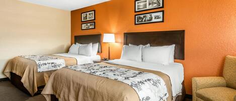 A hotel room with two beds, a chair, and framed pictures on the wall.