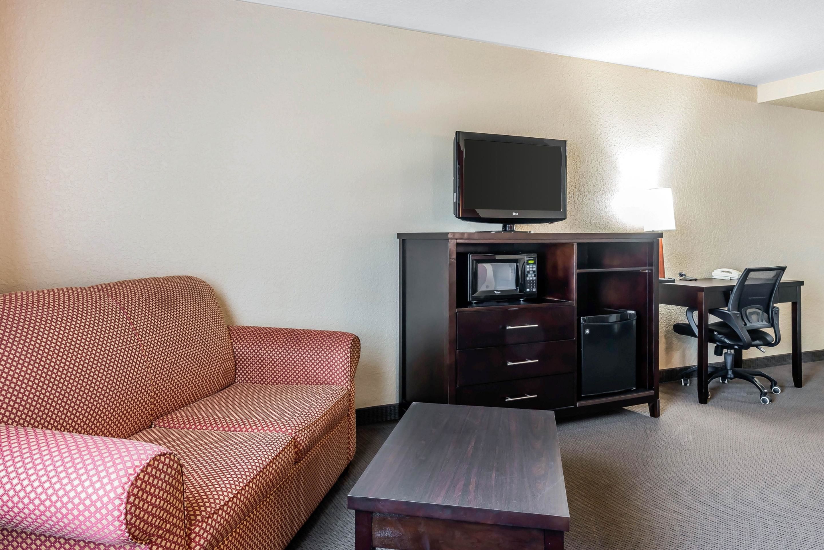 A hotel room with a sofa, a desk with a computer, a television, and a microwave.