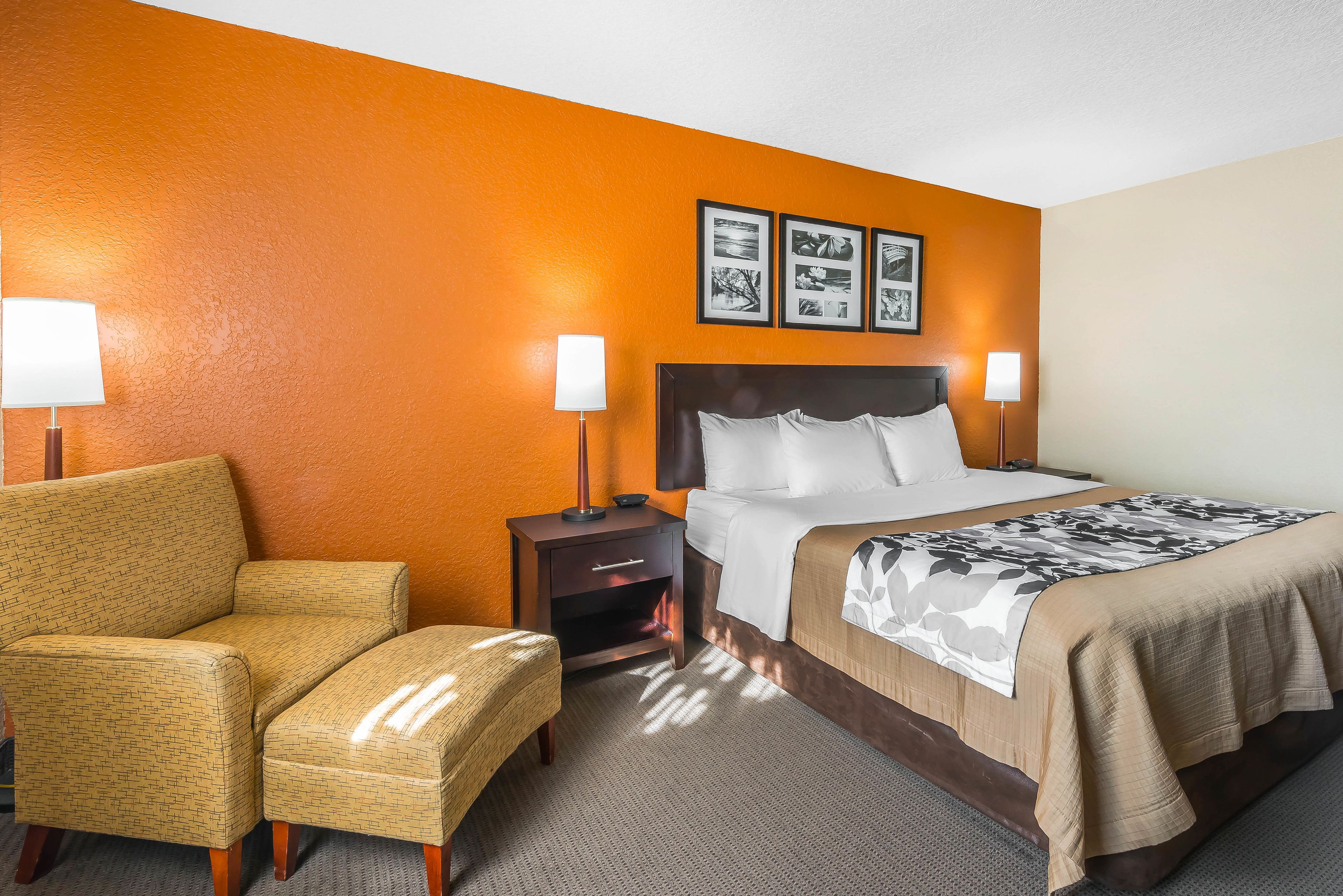 A hotel room with a bed, two bedside tables with lamps, a chair, and a wall with three framed pictures.