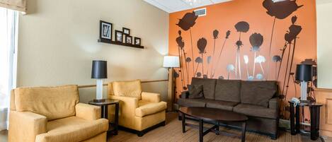 Ein Hotelzimmer mit beigeem Teppich, einer braunen Couch, zwei Sesseln, einem Couchtisch und einer Wand mit einem floralen Wandbild.