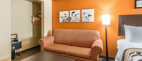 Una habitación de hotel con un sofá anaranjado estampado, una mesa de centro de madera, una cama con colcha estampada y una obra de arte colgada en la pared.