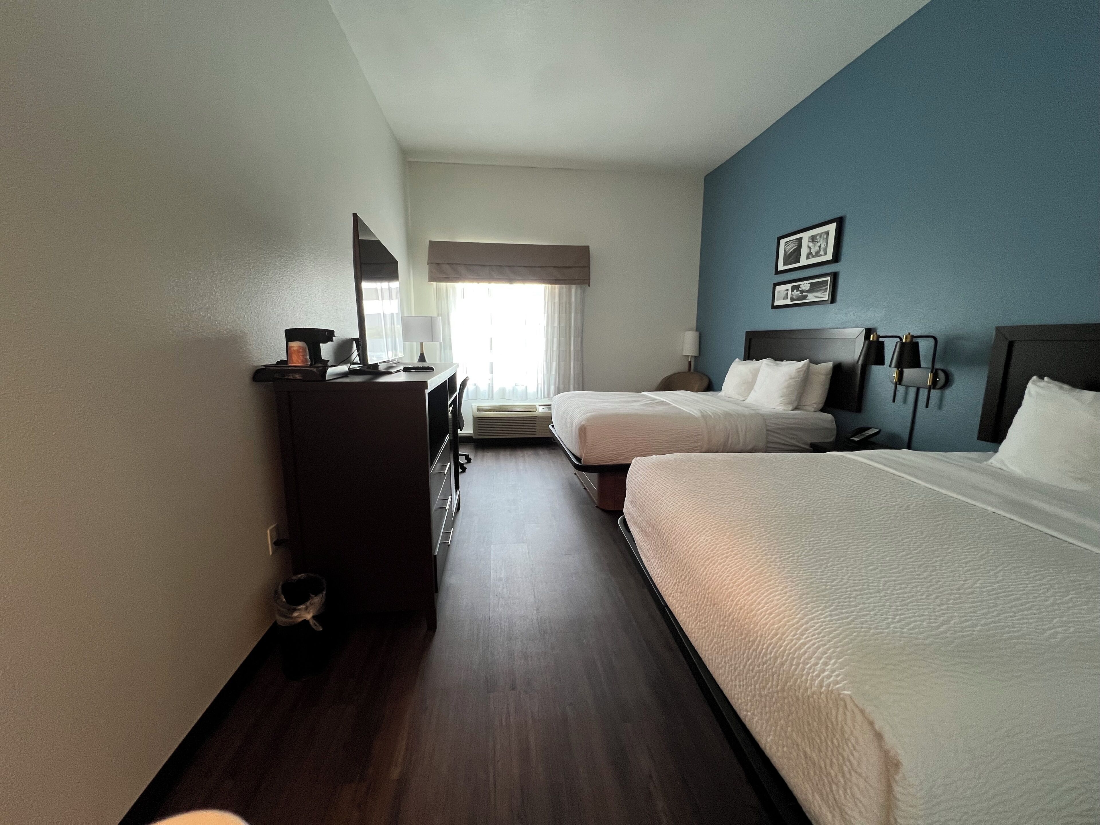 A hotel room with two beds, a desk, a chair, a lamp, and a window with curtains.