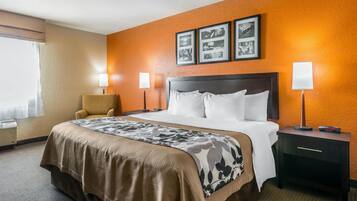 Una habitación de hotel con una cama grande, dos lámparas de noche, una silla y una mesita de noche con un reloj.