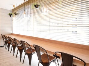 A room with a long wooden bench, metal chairs, and a wall with blinds and hanging plants. - Comfort Hotel Tokyo Kiyosumi Shirakawa (Tokyo)