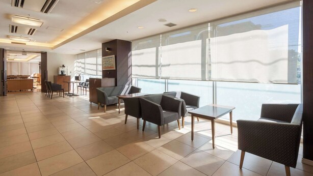 Un hall d’entrée spacieux, doté de meubles modernes, de grandes fenêtres et d’un espace cuisine visible.
