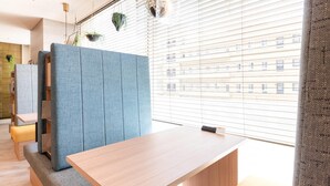 Une pièce moderne et bien éclairée, avec une table en bois, des sièges bleus et une vue sur les bâtiments à travers de grandes fenêtres.