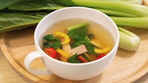 Une tasse blanche remplie d’un liquide transparent et de divers légumes, le tout posé sur un plateau en bois.
