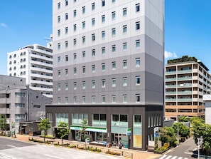 Et hotel med flere etager, moderne facade, store vinduer og en FamilyMart døgnbutik i stueetagen.