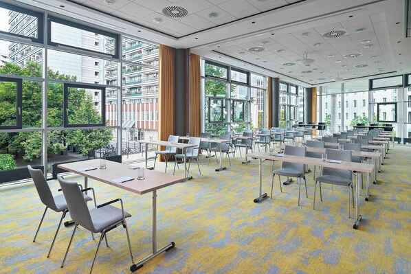 Un salón de conferencias moderno con ventanas amplias, varias mesas y sillas.