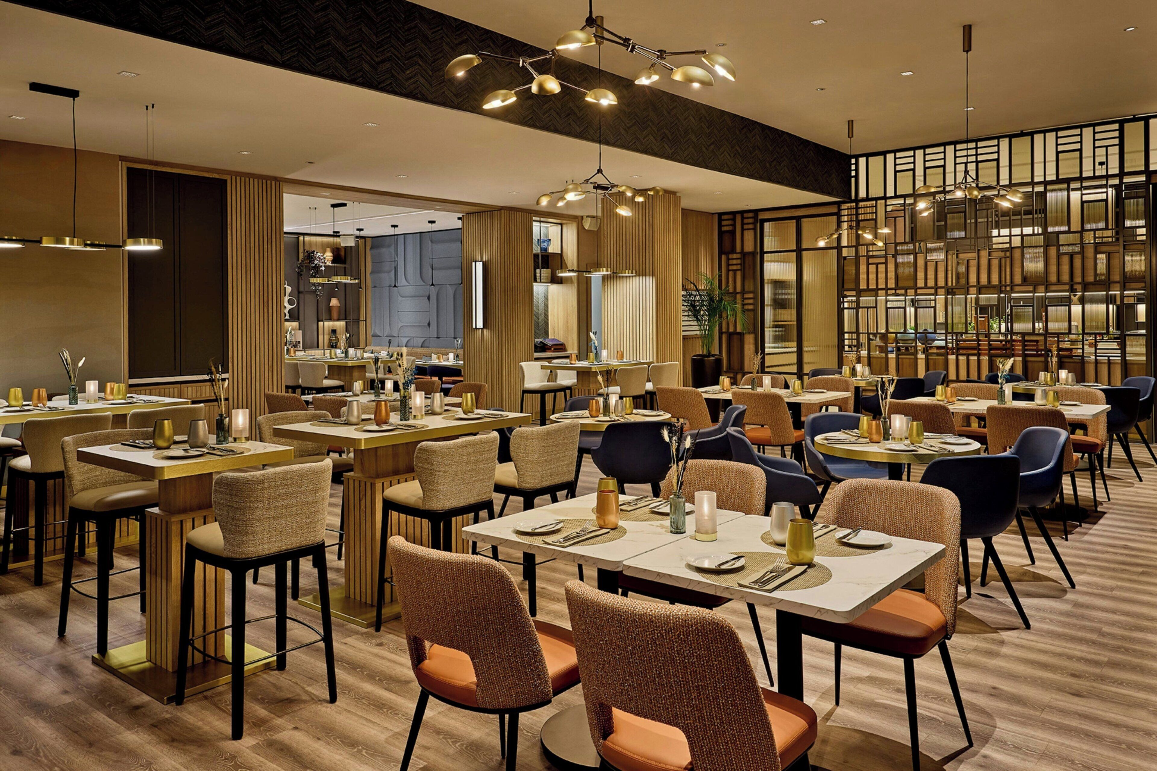 Ein modernes Restaurant mit mehreren Tischen und Stühlen, stimmungsvoller Beleuchtung und einem zeitgemäßen Interieur.