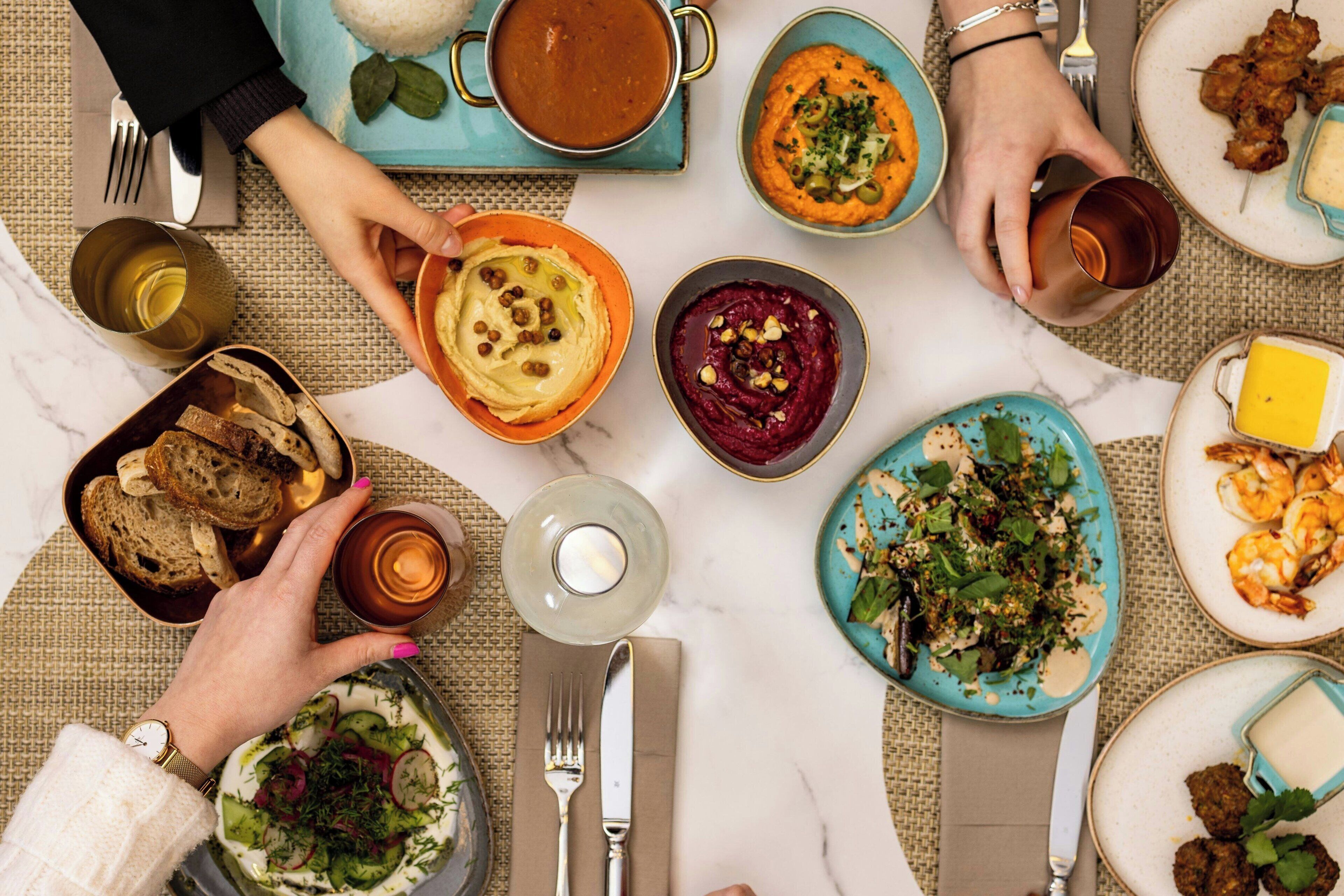 A table set with various dishes, including hummus, salad, and grilled shrimp, indicating a meal setting.