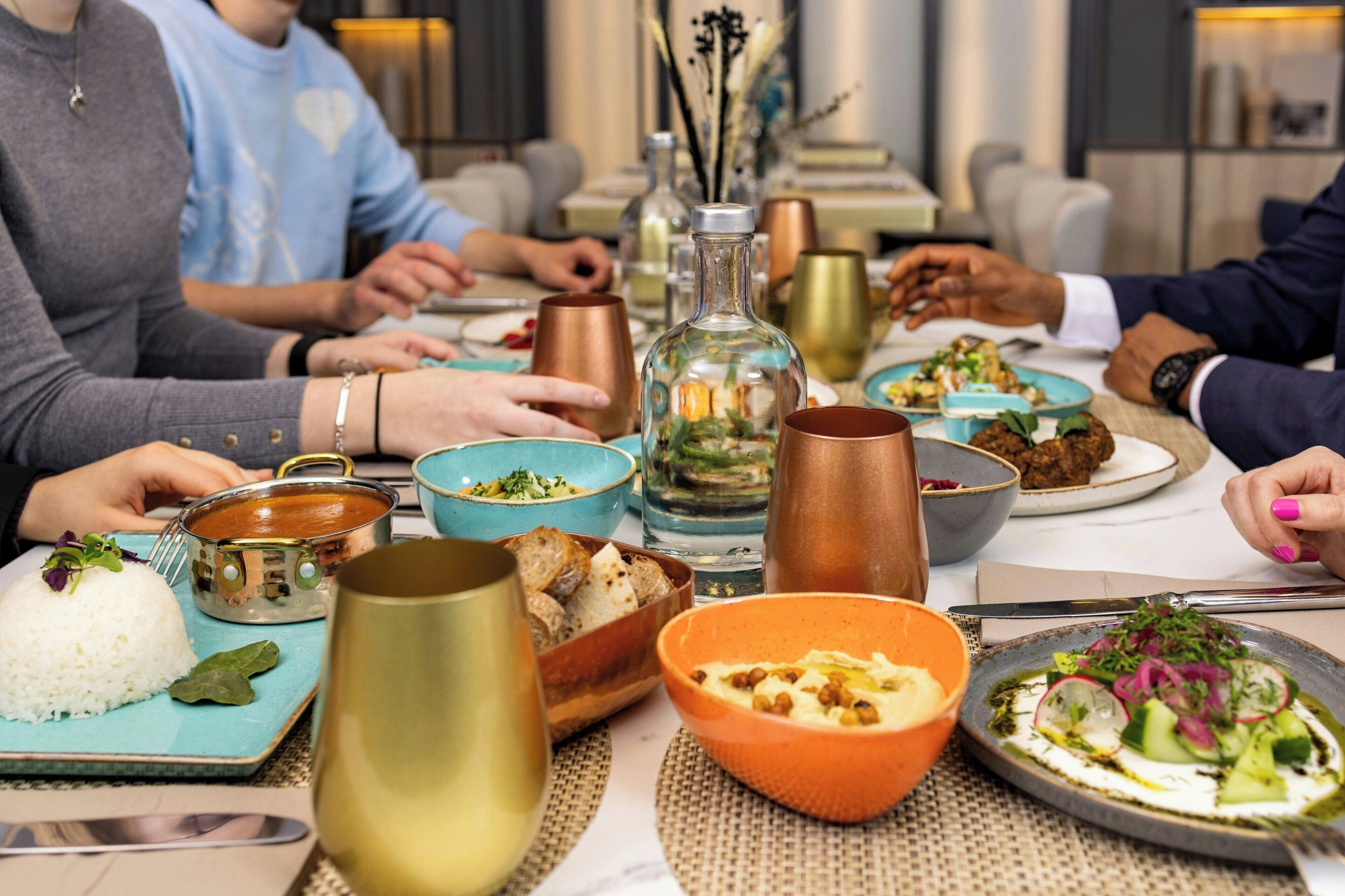 A dining table with various dishes, including rice, hummus, and a salad, and several decorative items like a glass bottle and copper mugs.