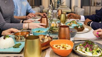 A dining table with various dishes, including rice, hummus, and a salad, and several decorative items like a glass bottle and copper mugs.