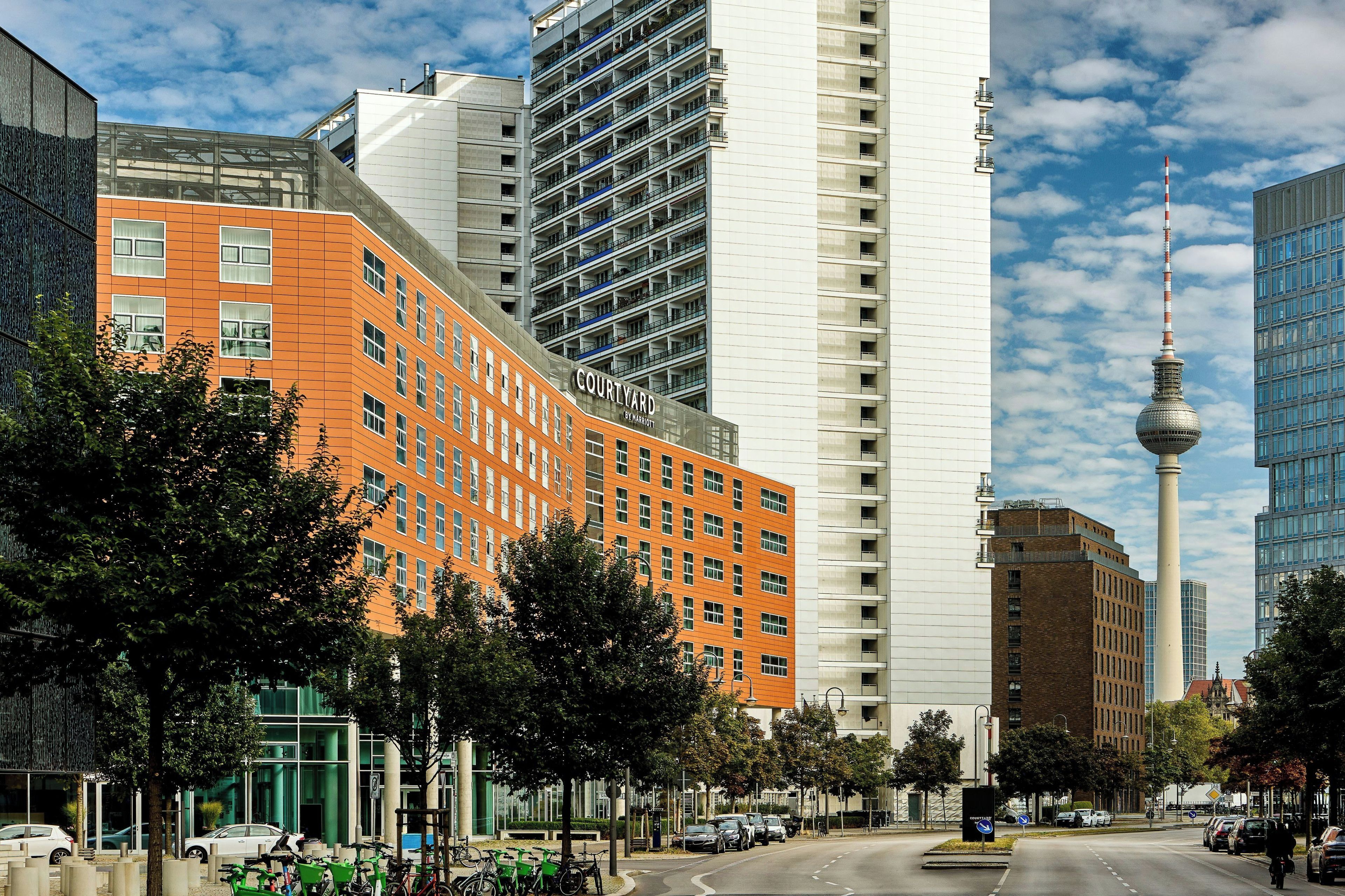 Un hotel de varios pisos con una fachada anaranjada llamativa, una estructura moderna de vidrio y vistas a un edificio alto con una torre distintiva.
