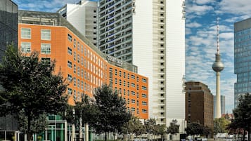 Un hotel de varios pisos con una fachada anaranjada llamativa, una estructura moderna de vidrio y vistas a un edificio alto con una torre distintiva.