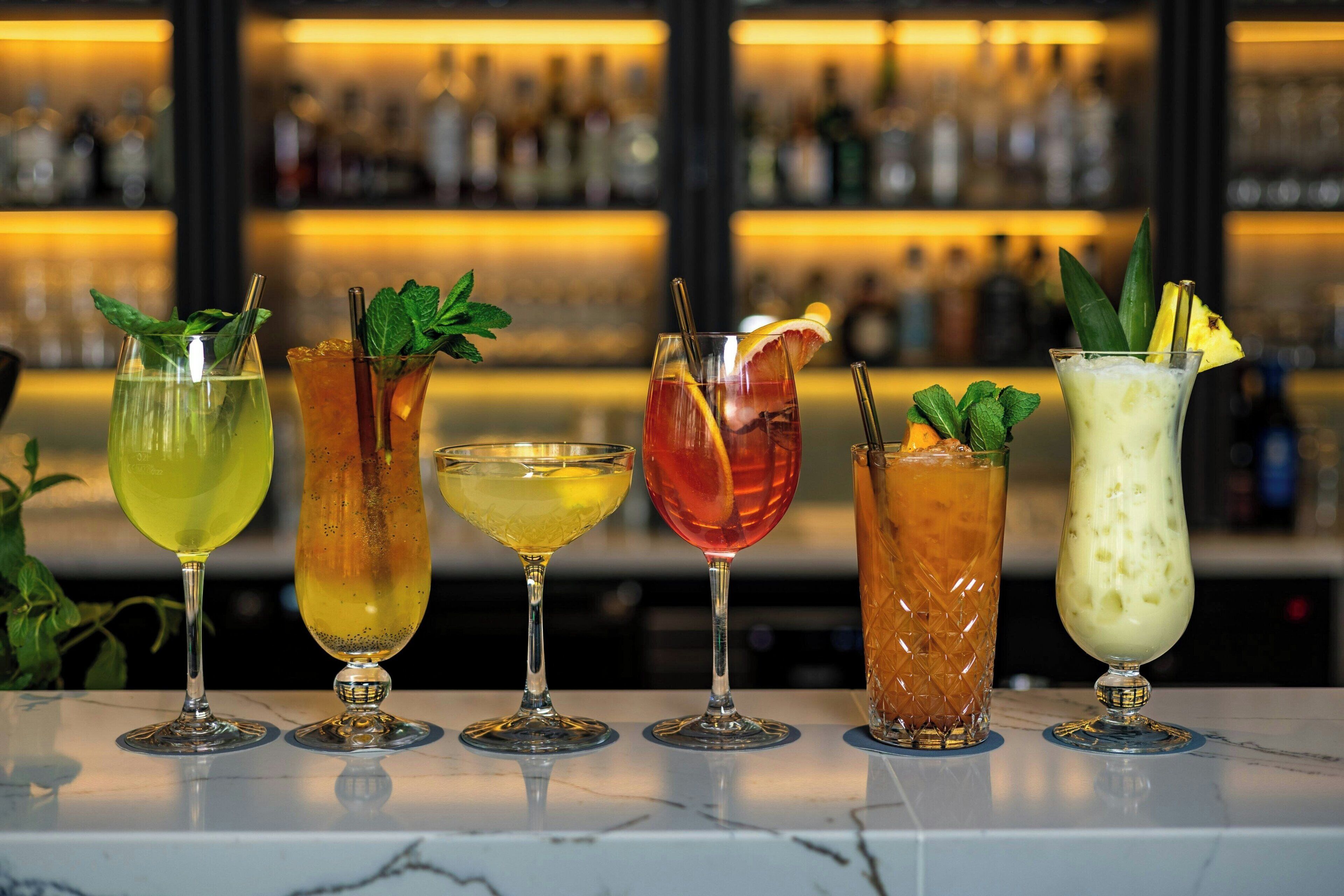 Un bar con seis cócteles diferentes, cada uno decorado con diversas frutas y hierbas.