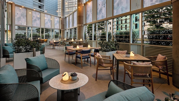 Een ruime, overdekte patio met meerdere zithoeken, waaronder banken en tafels, omringd door grote ramen met uitzicht op de skyline.