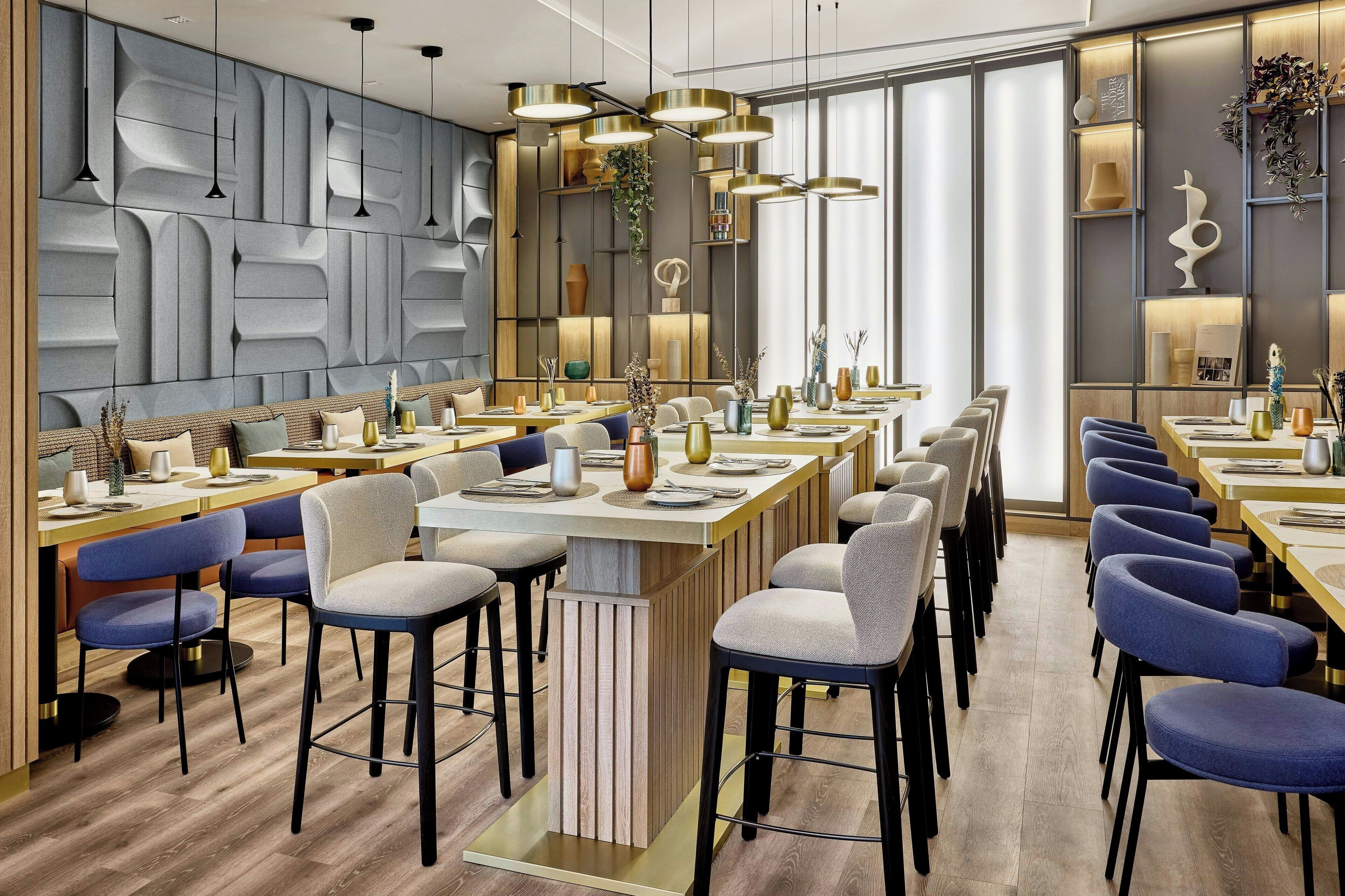 Un espace de restauration moderne, doté de plusieurs tables et chaises, d’un mur décoratif et d’un éclairage suspendu.