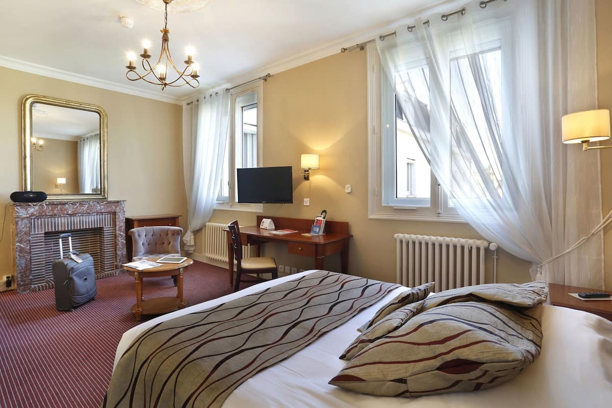 Habitación de hotel con cama, escritorio, silla, televisión, chimenea y un espejo grande.