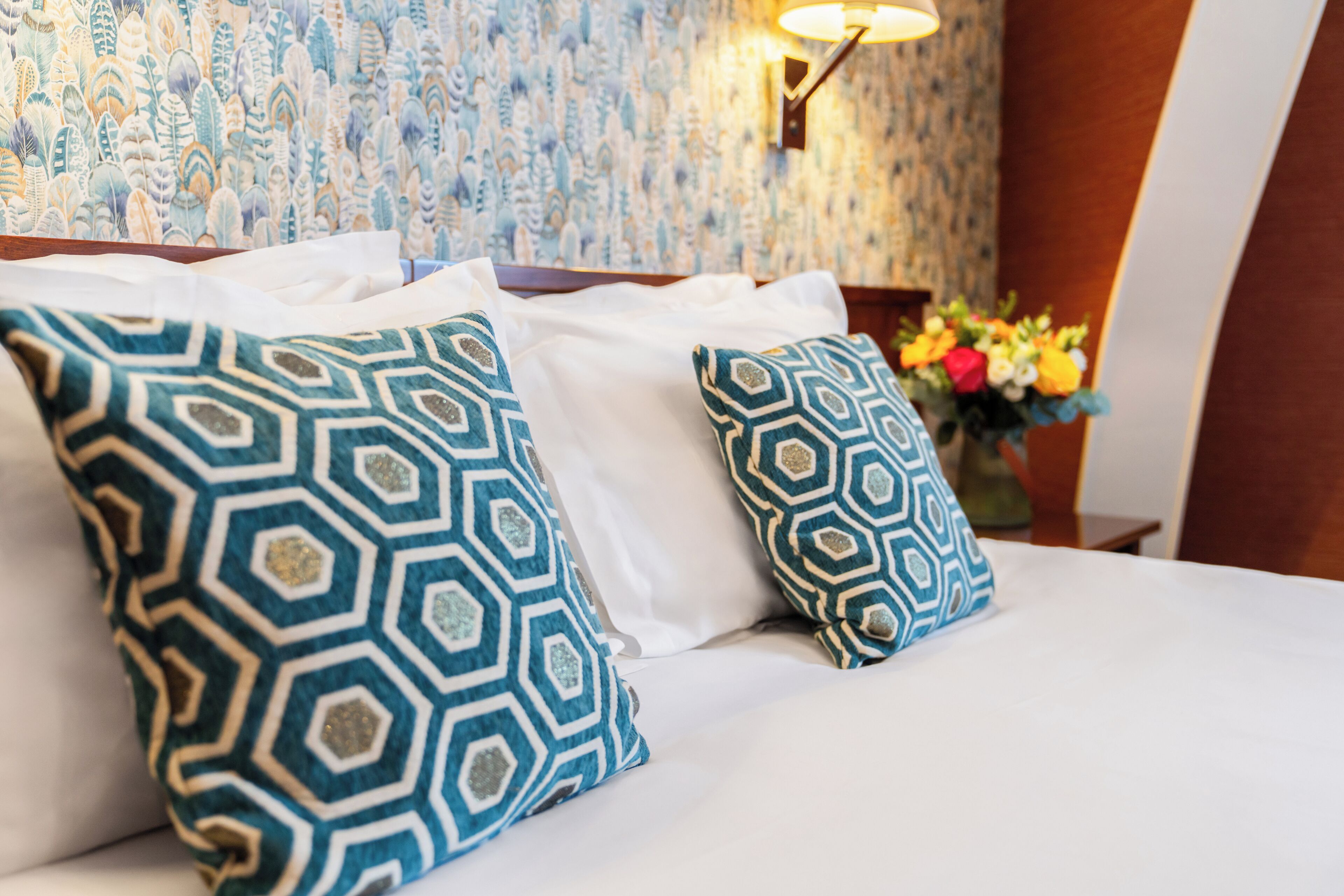 A neatly made bed with patterned pillows and a vase of flowers on a nightstand.