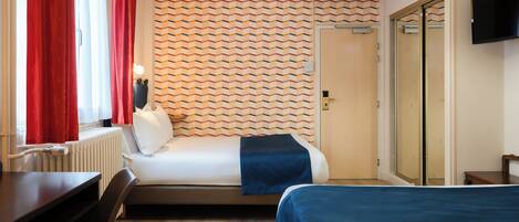 A hotel room with a bed, a desk, a chair, a radiator, a television, and a door with a mirror.