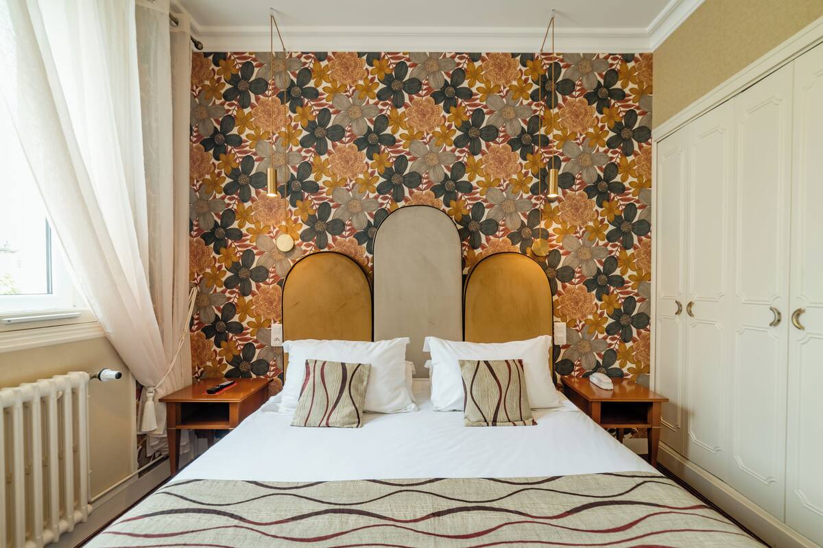 Una habitación de hotel con una cama grande, un papel tapiz floral y un armario.