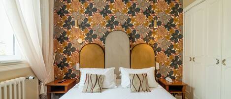 A hotel room with a large bed, a floral wallpaper, and a wardrobe.