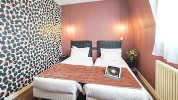 A double bed with a laptop, two bedside tables, a vase with flowers, and a patterned wallpaper.