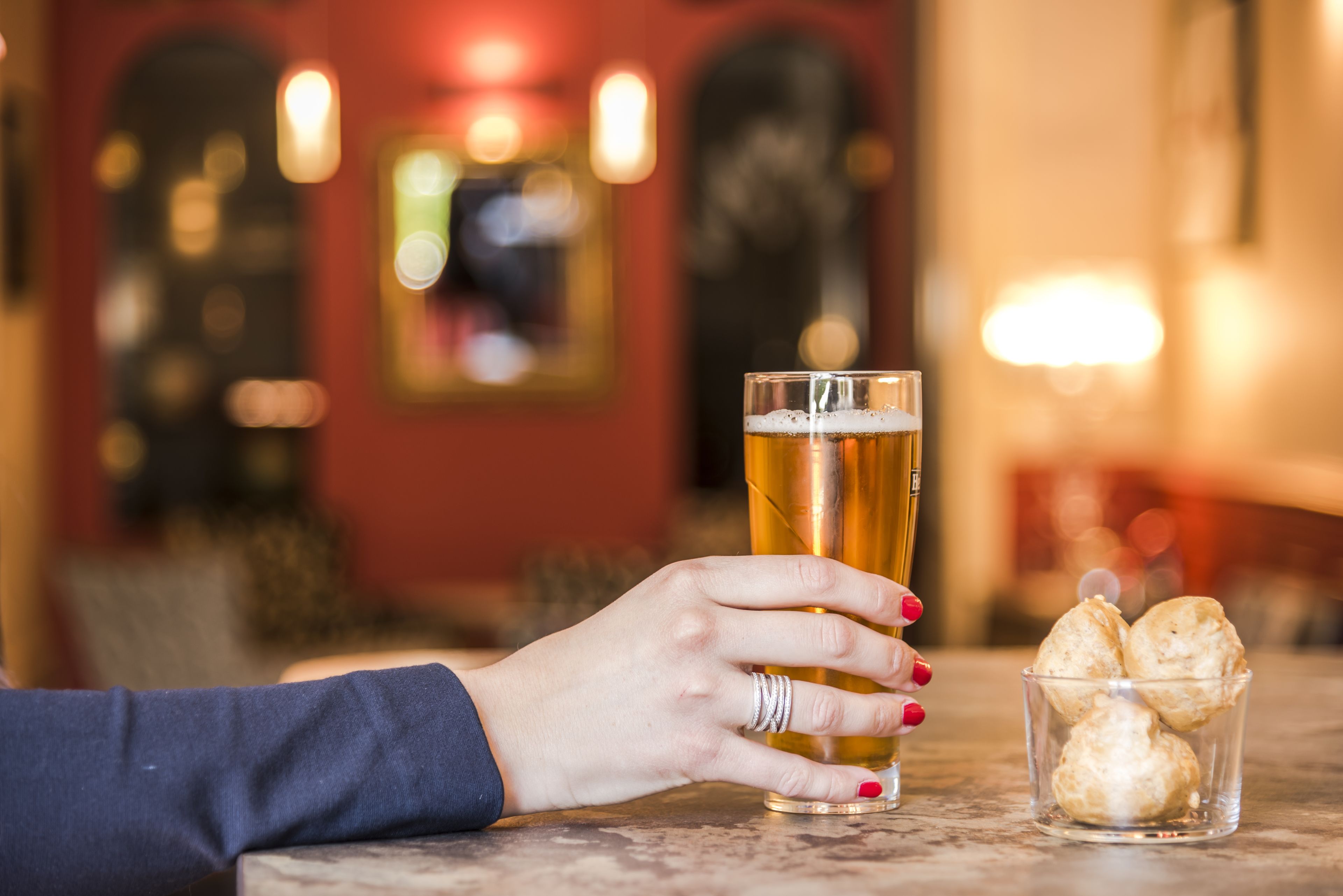 A hand holding a glass of beer next to a glass of beer and a small glass of biscuits.