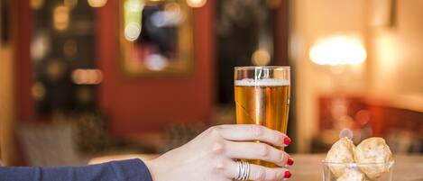 A hand holding a glass of beer next to a glass of beer and a small glass of biscuits.