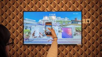A person using a smartphone to scan a QR code on a screen displaying a hotel interior.