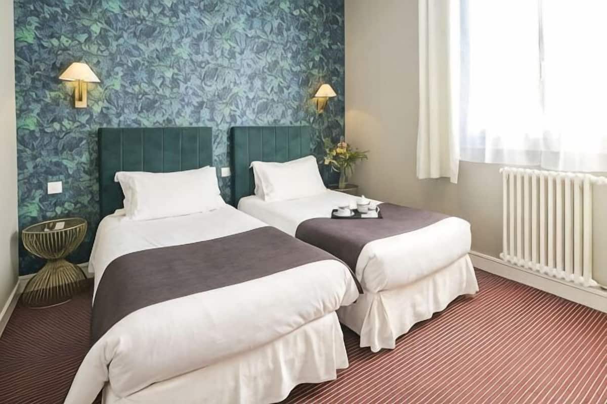 Quarto de hotel com duas camas, um radiador e duas luminárias fixadas na parede.