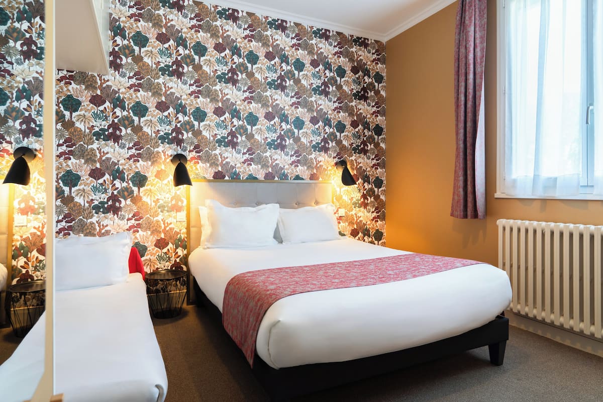 Habitación de hotel con cama, dos mesitas de noche, cabecero, radiador y ventana con cortinas.