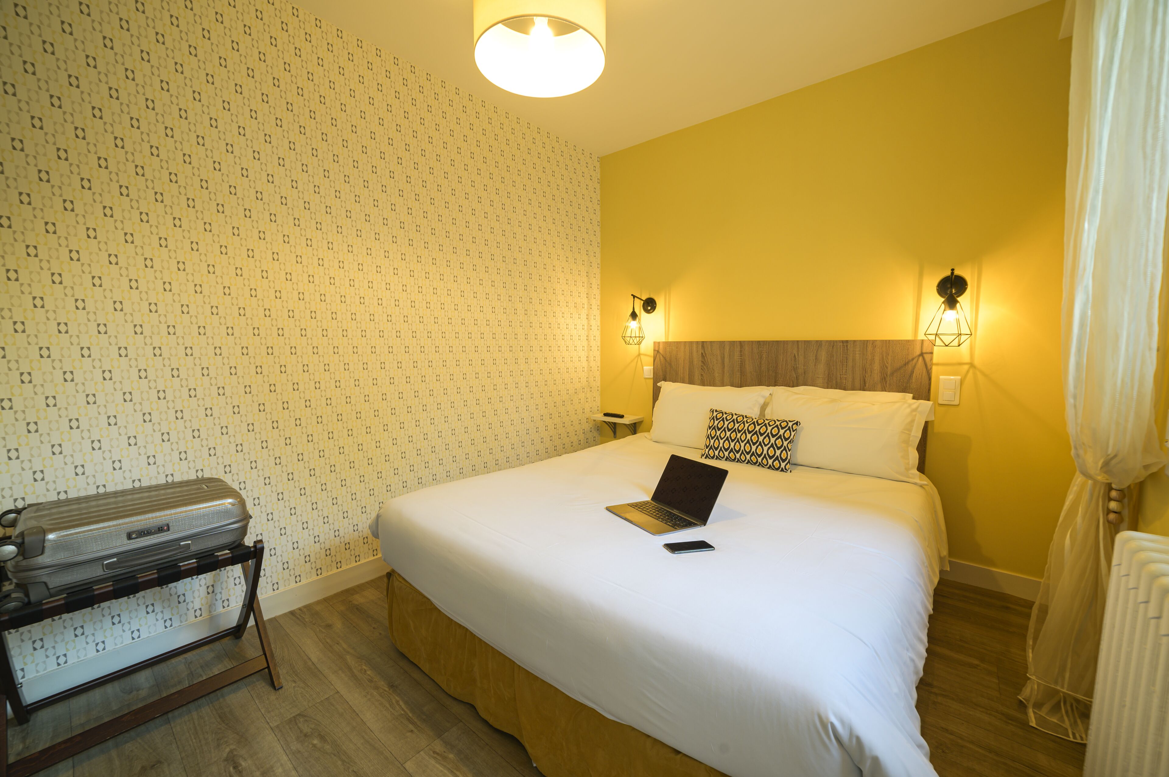 Une chambre d’hôtel avec un lit, une valise, un ordinateur portable et un téléphone intelligent posés sur le lit.
