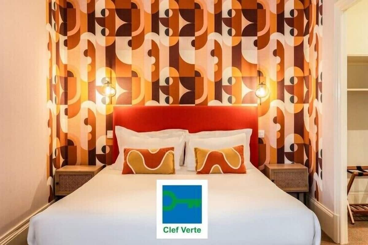 Una habitación de hotel con papel tapiz estampado, un cabecero rojo y dos lámparas de noche.
