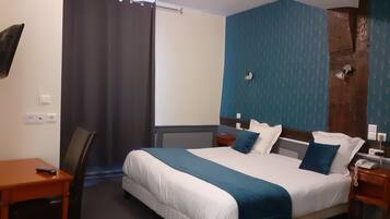 A hotel room with a large bed, a desk, a chair, a TV mounted on the wall, and a bathroom with a shower.