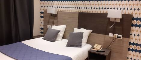Habitación de hotel con una cama, dos mesitas de noche, un teléfono y una pared con diseño geométrico.