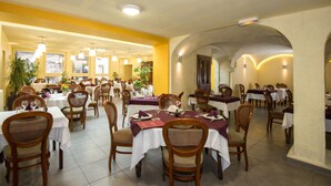 Um restaurante com várias mesas e cadeiras, paredes amarelas e luminárias no teto.