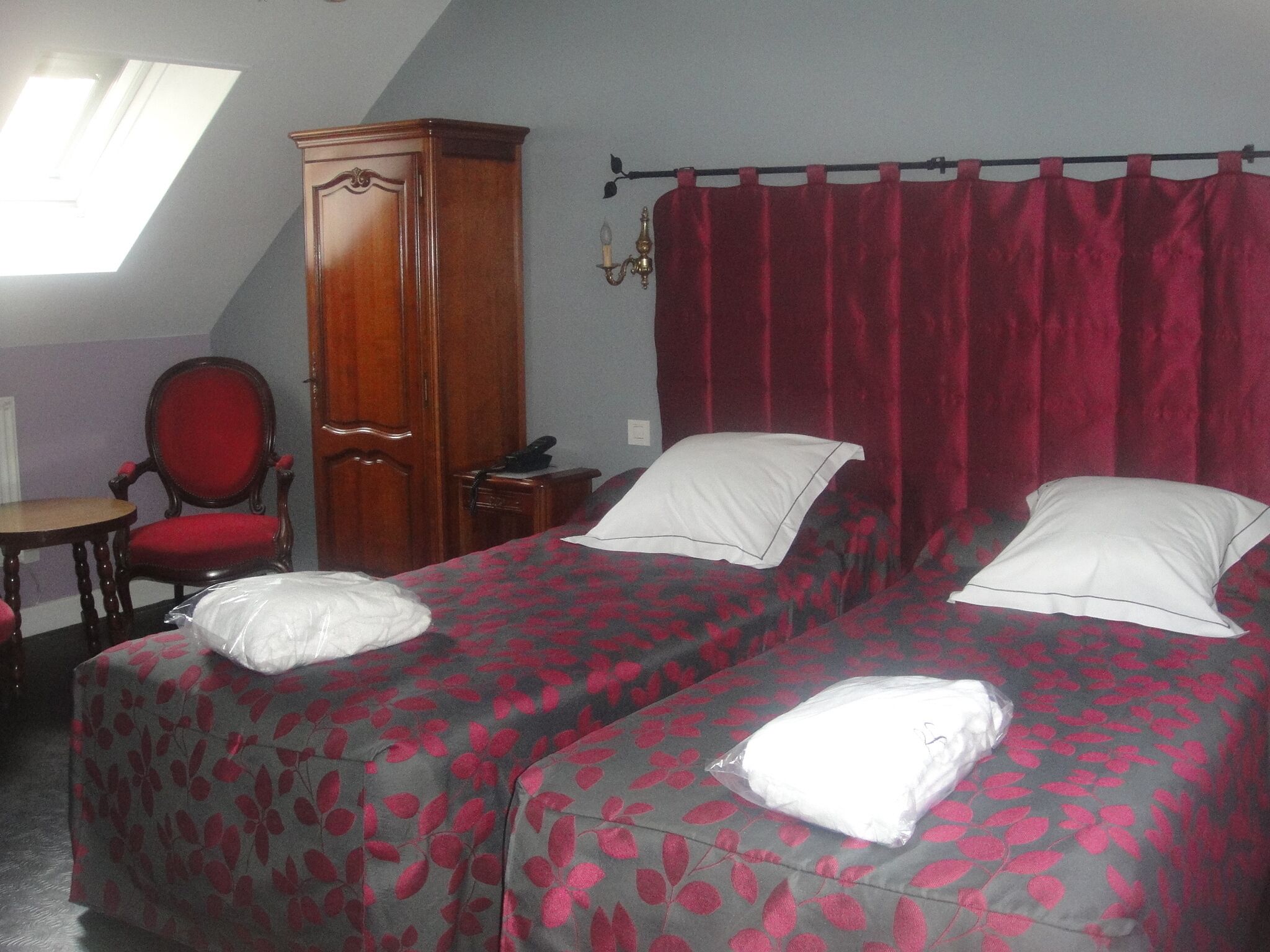Une chambre avec deux lits, une armoire en bois, une chaise rouge et une petite table.