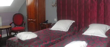 A room with two beds, a wooden wardrobe, a red chair, and a small table.