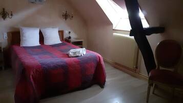 A bedroom with a bed, a chair, a nightstand, a lamp, a radiator, and a window.
