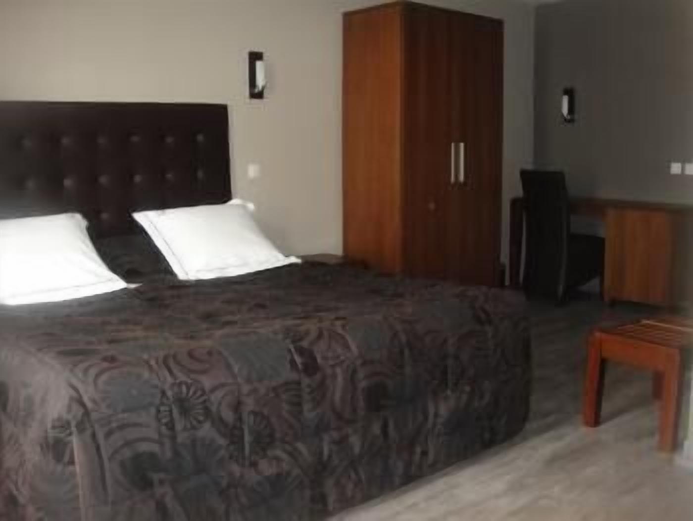 A bedroom with a large bed, a wooden wardrobe, and a desk.