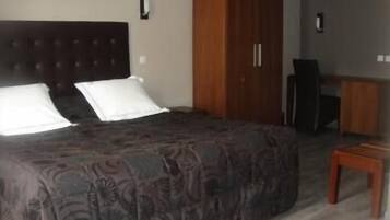 A bedroom with a large bed, a wooden wardrobe, and a desk.