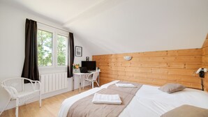 Un dormitorio con cabecera de madera, cama con edredón blanco, escritorio con computadora y una silla blanca.
