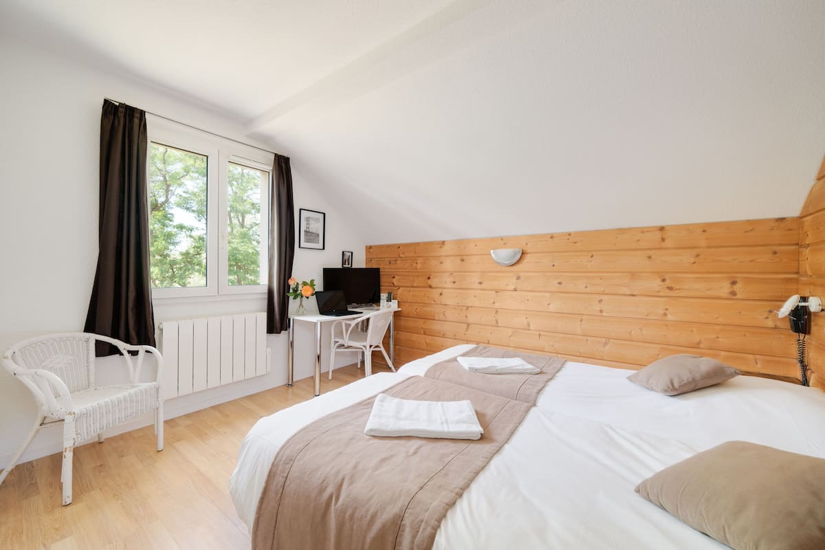 A bedroom with a wooden headboard, a bed with a white comforter, a desk with a computer, and a white chair.