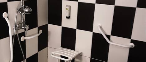 Un baño con piso a cuadros blanco y negro, un inodoro blanco y una ducha con cabezal de mano.