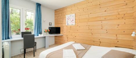 A bedroom with a wooden wall, a bed with a brown pillow, a desk with a computer, and a window with curtains.