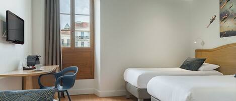Habitación de hotel con cama, escritorio con silla, televisor y ventana con cortinas.