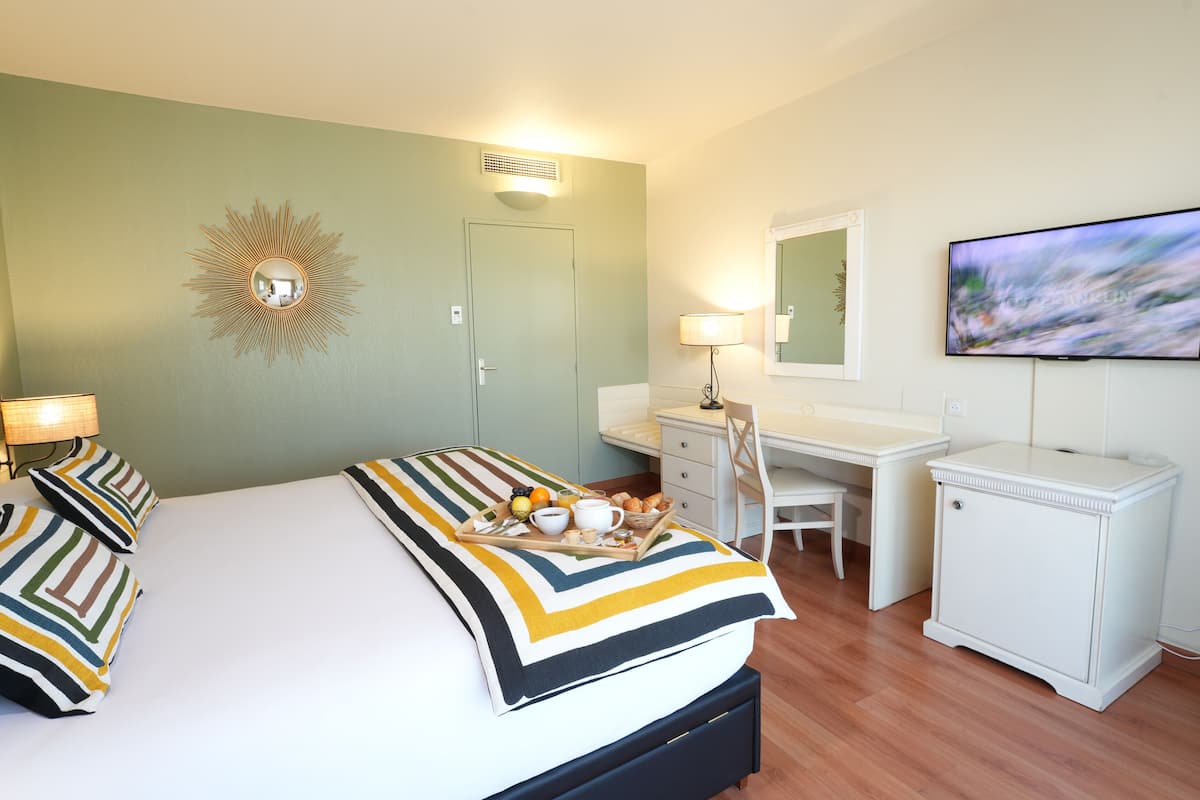 A hotel room with a bed, a desk, a chair, a TV, and a breakfast tray on the bed.