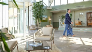 Un espacio interior amplio con un gran ventanal que da al exterior, mobiliario de mimbre y una planta en maceta.
